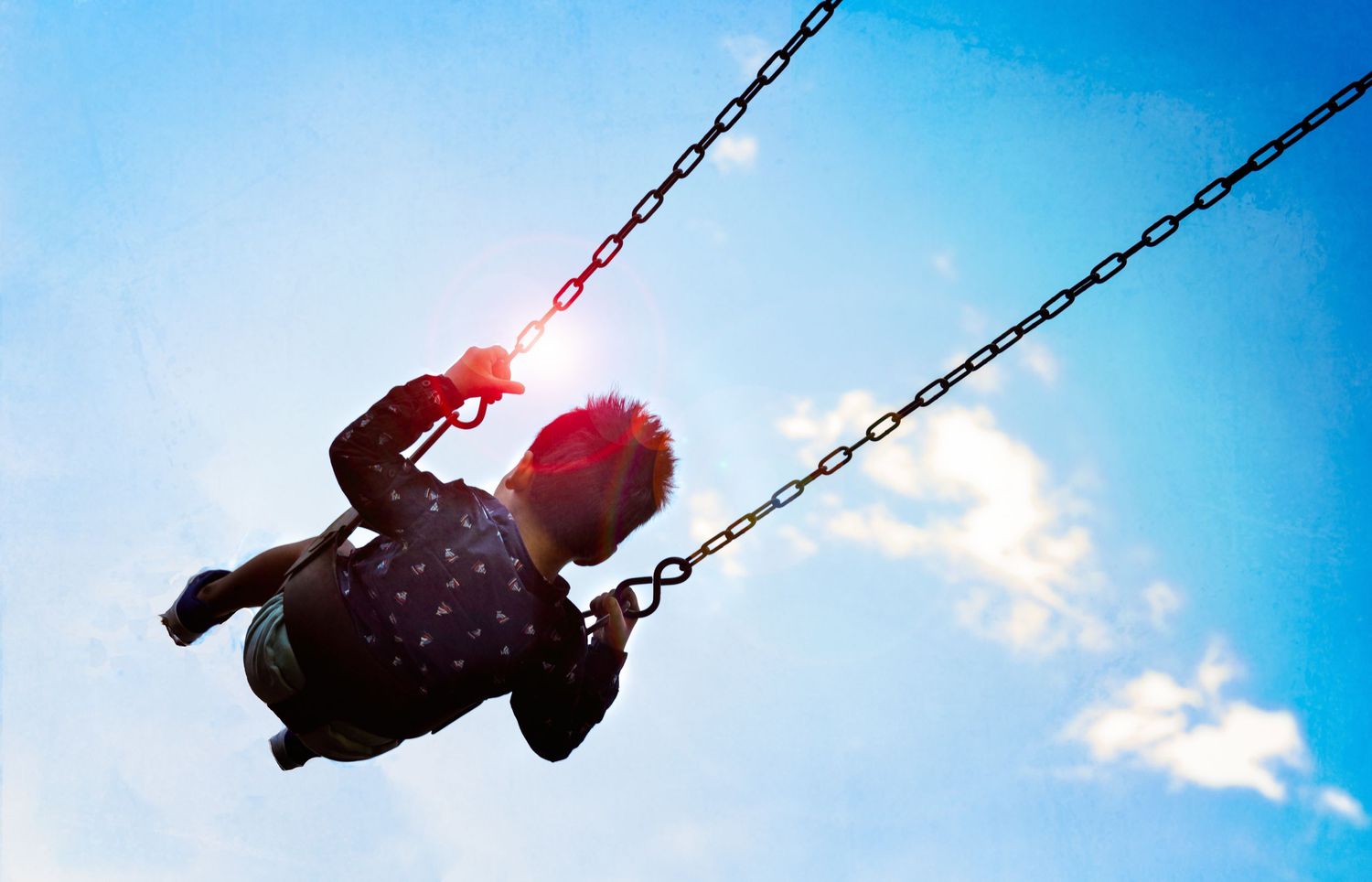 little kid enjoying in the sun on the swing which appears to be reaching for the sky