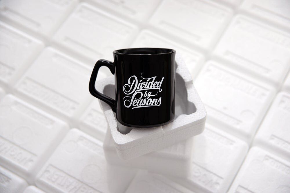 Black and white coffee mugs with typography arranged on white tiled surface.