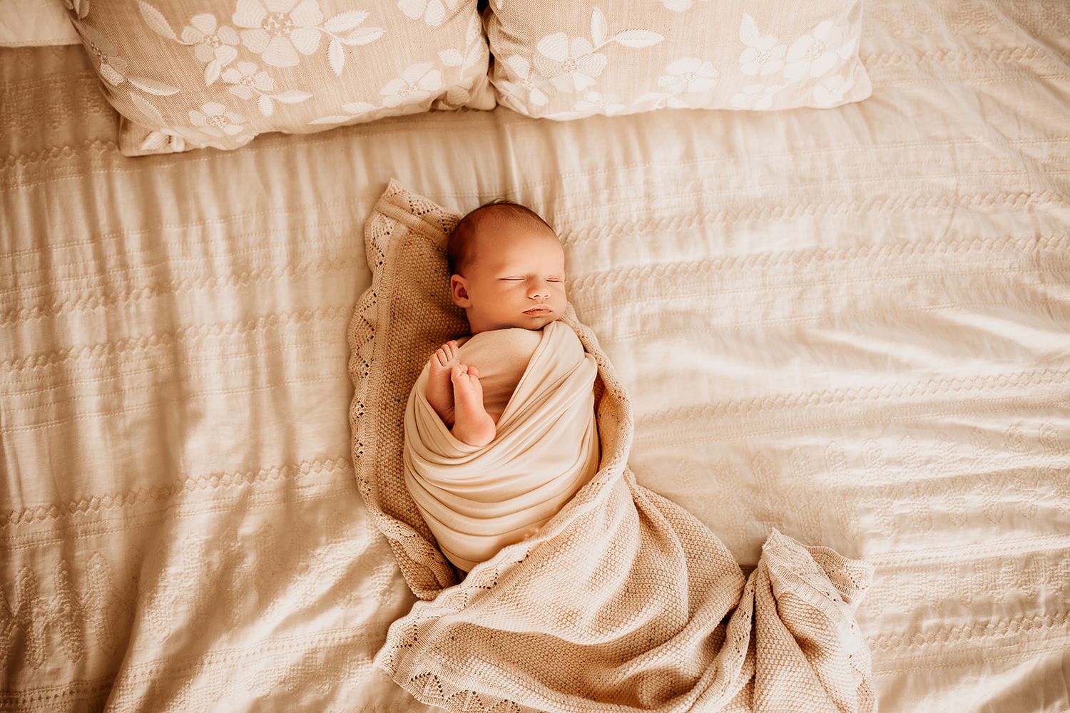 A newborn baby boy lays swaddled on his parent's bed during their newborn photo session.