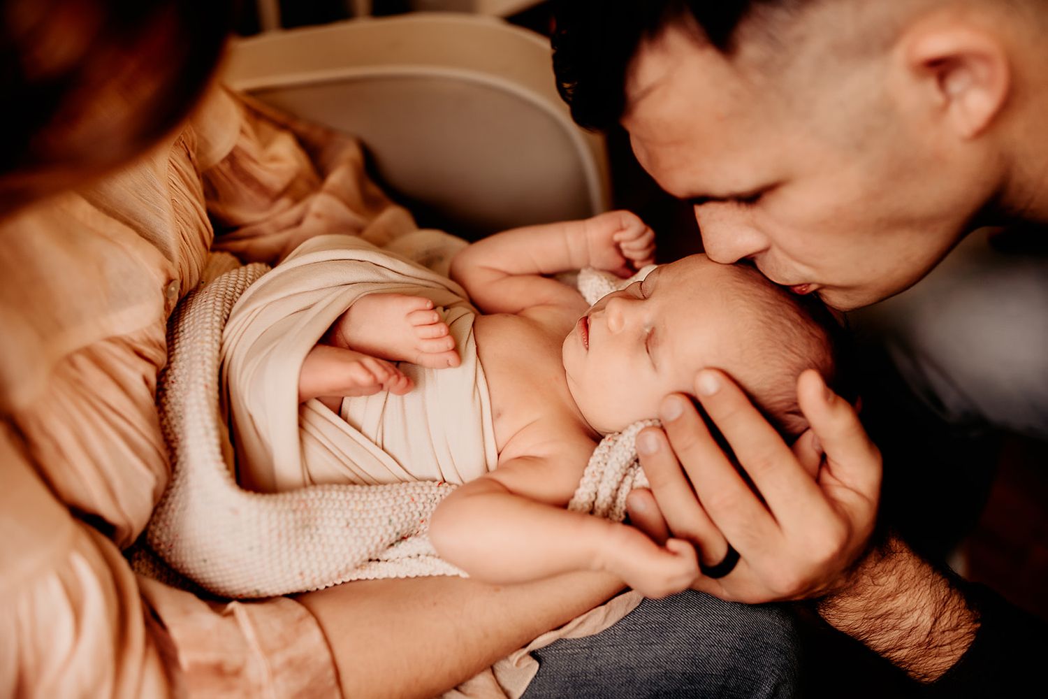 A new father leans down to kiss the top of his newborn baby's head.
