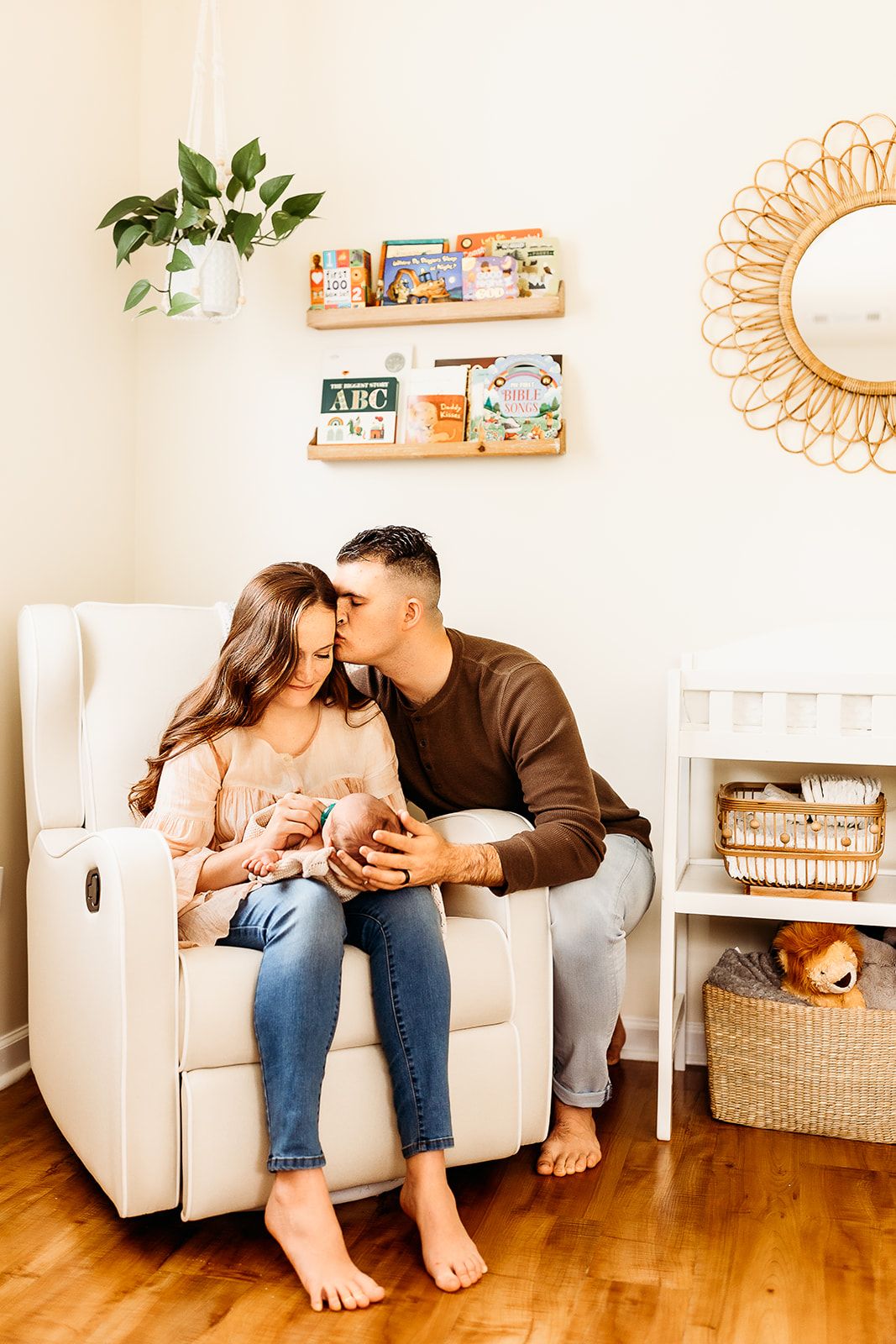 A man kisses his wife's head while they hold their baby boy in his nursery.