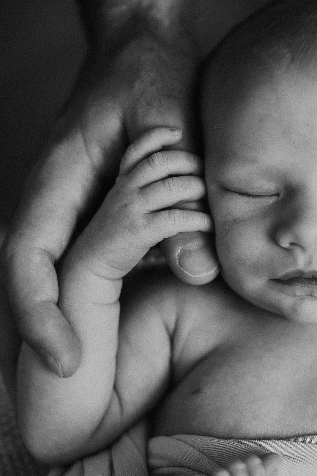 A newborn baby holds on tight to his fathers thumb.