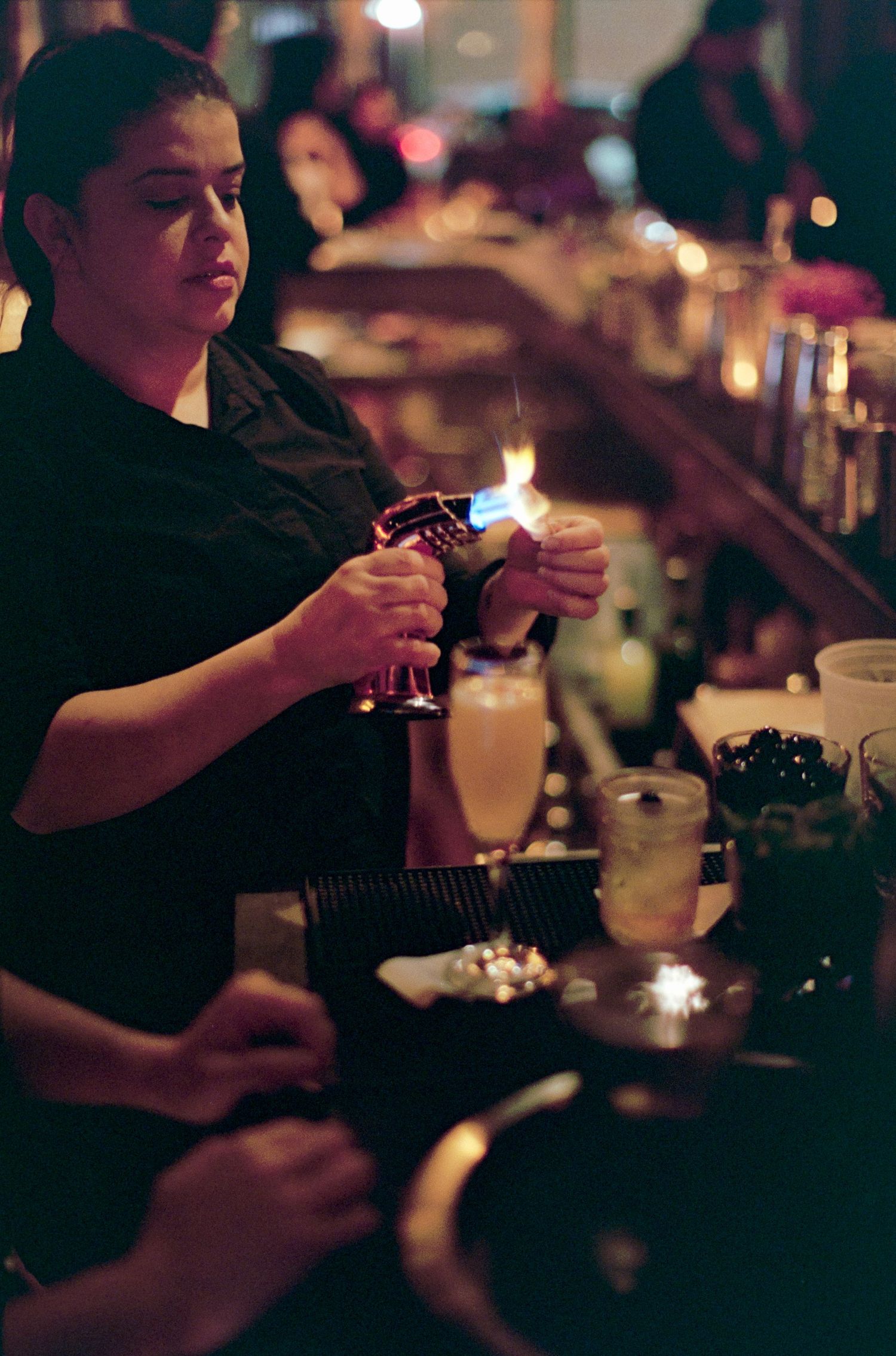 Bartender mixing drinks at a dimly lit bar counter with glassware.