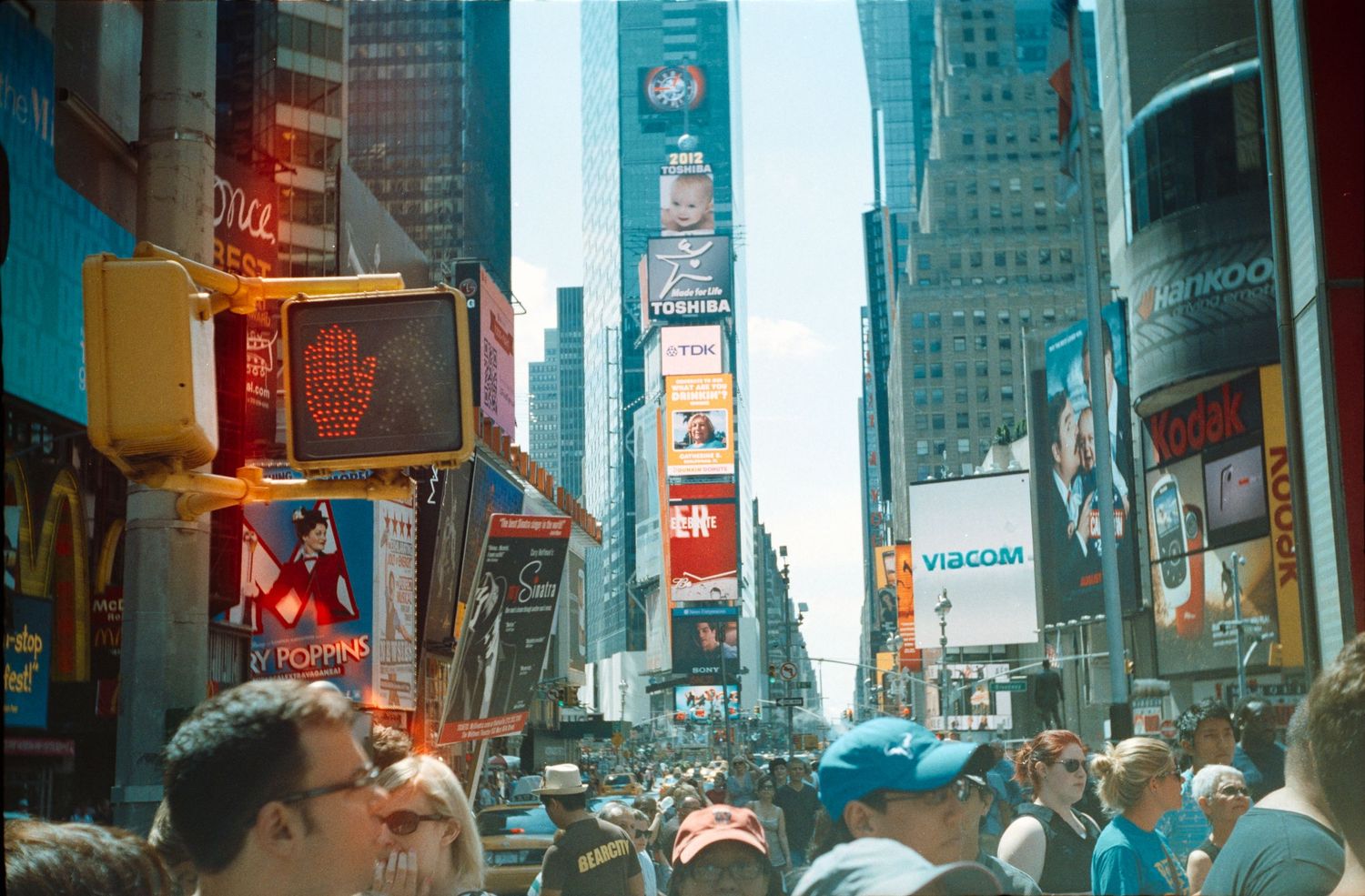 Crowded Times Square in New York City with bright billboards and tall buildings.
