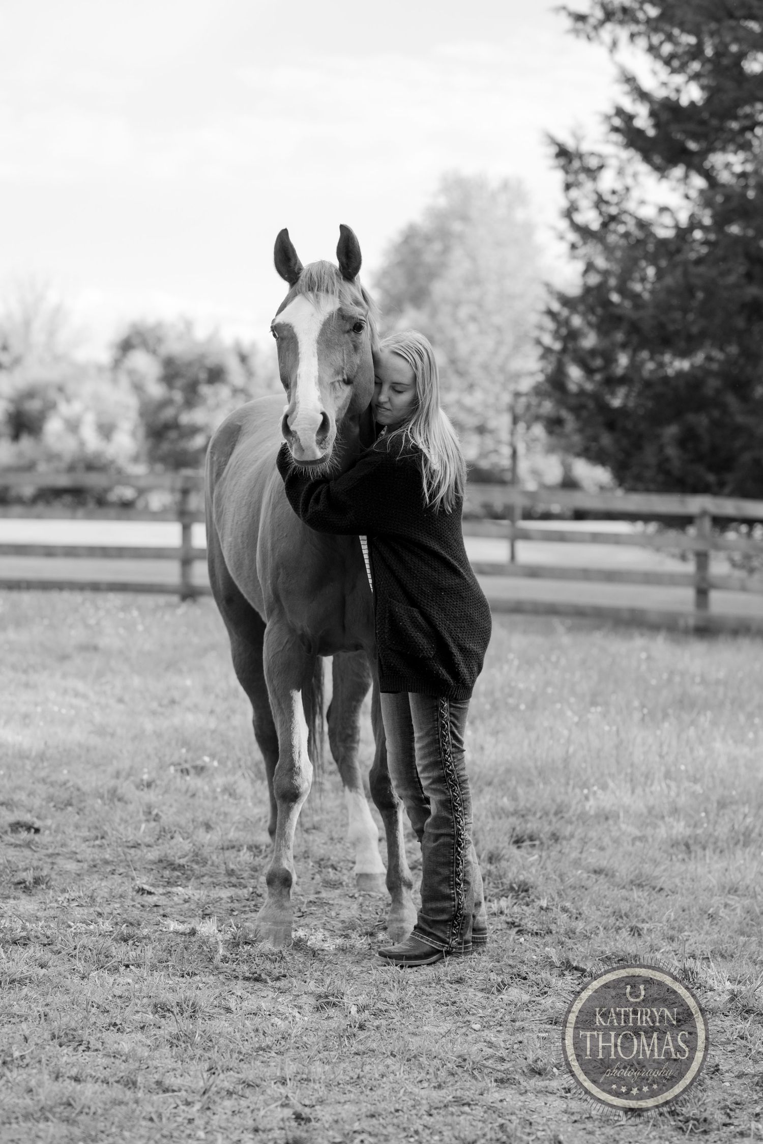 A gentle moment between a light-colored horse and person in boots standing together in a pasture.