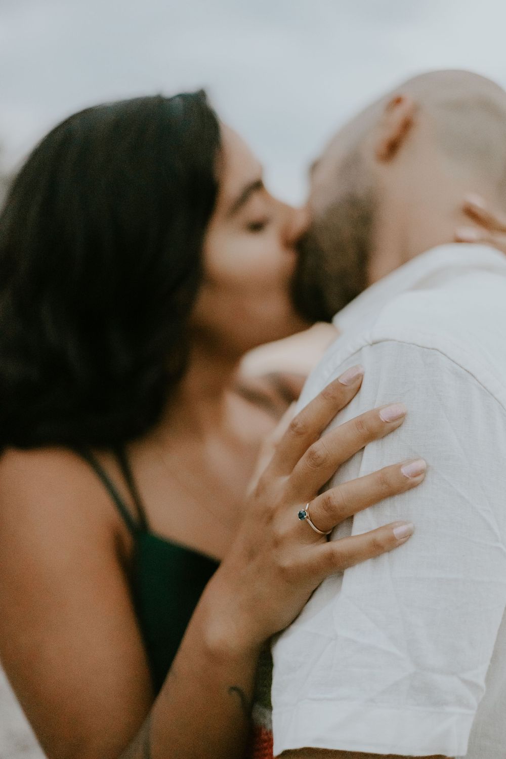 A tender kiss shared between a couple on a rocky shoreline at dusk.