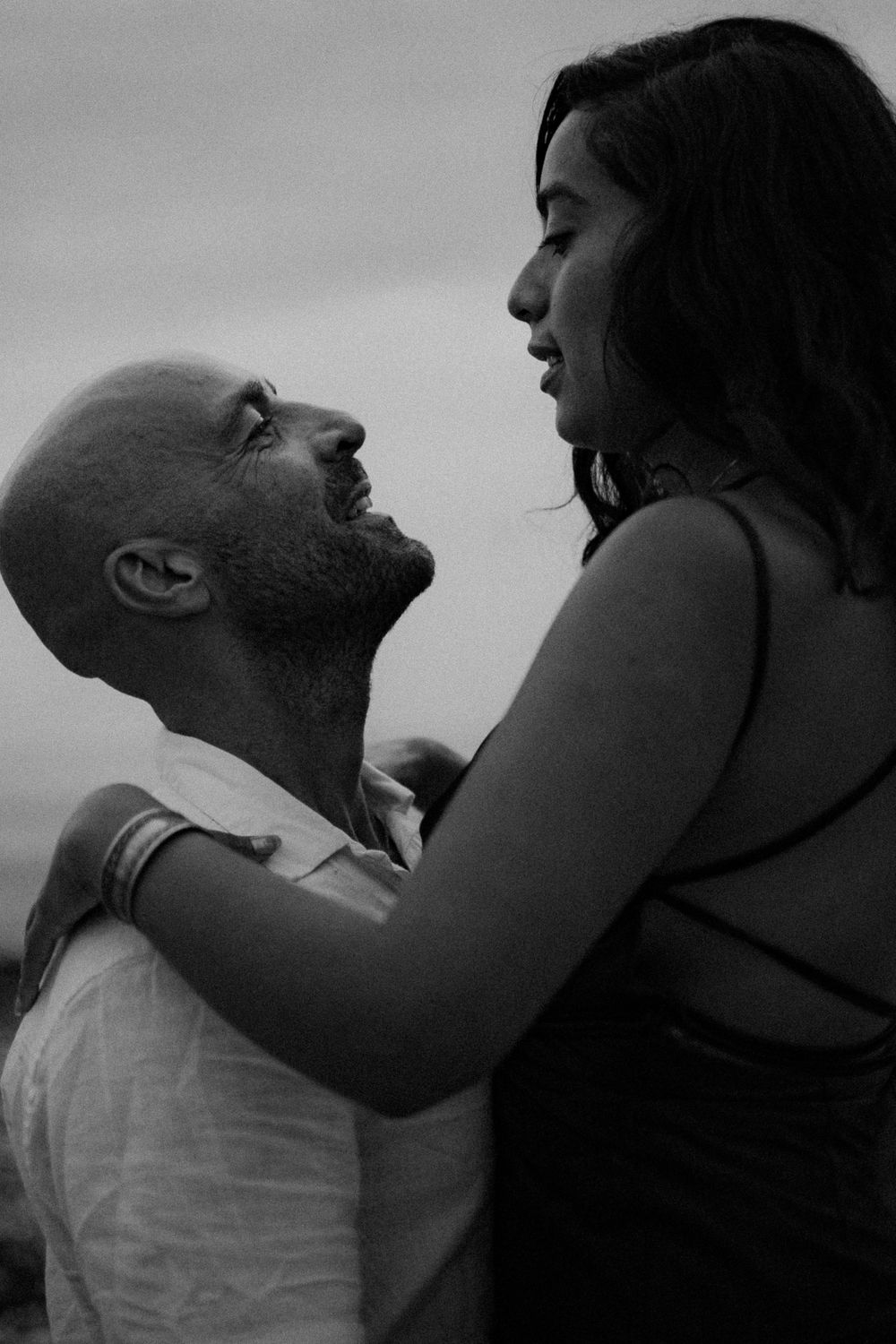A black and white portrait of a couple sharing an intimate moment on the shore.