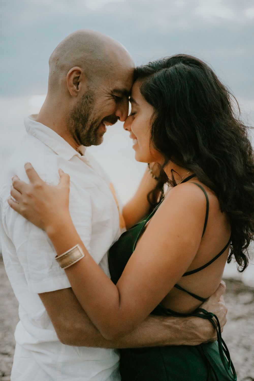 A candid moment of a couple sharing a tender smile on the beach at sunset.