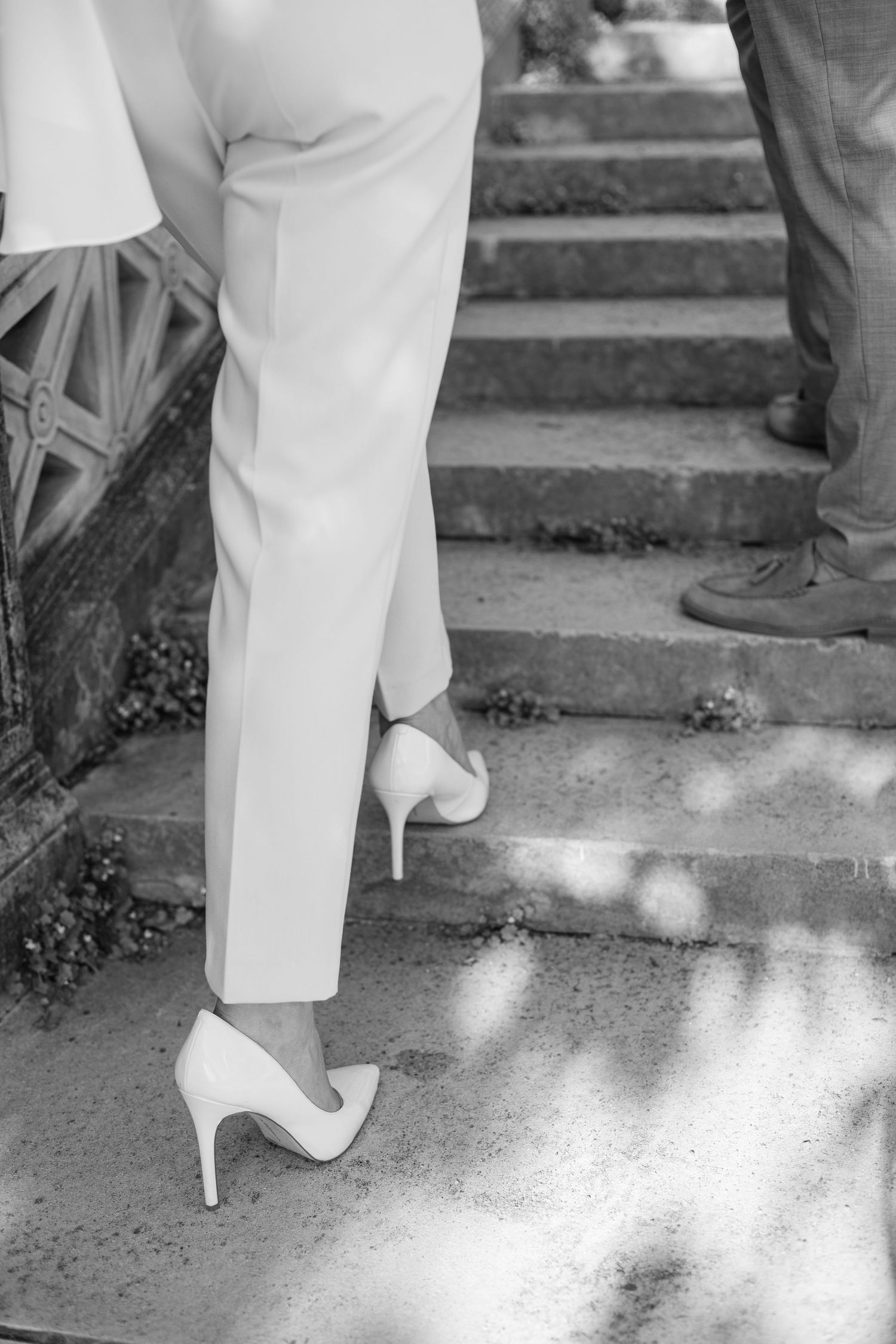 Black and white detail shot of white heels on stone steps in dappled sunlight.