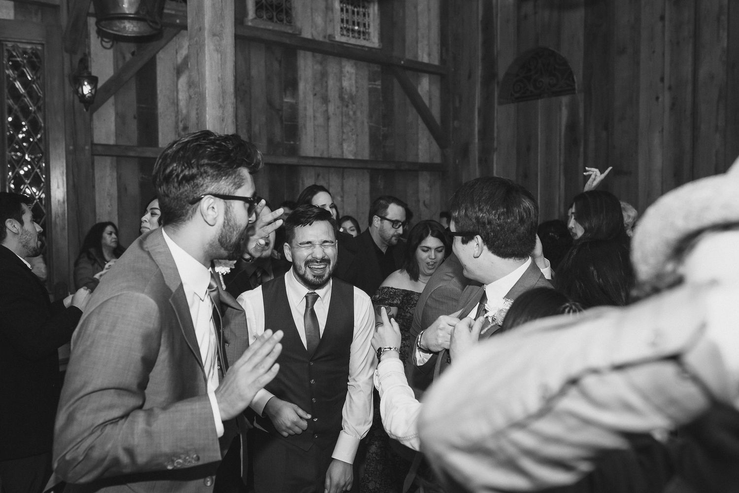 Black and white photo of guests celebrating and dancing at an indoor wedding reception.