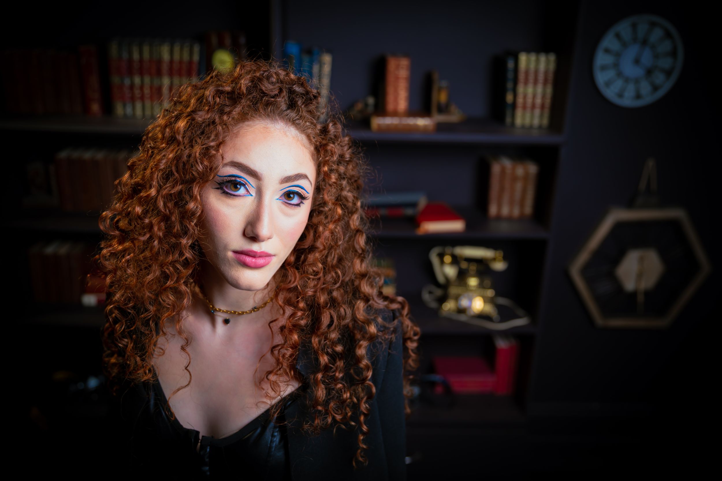 Dramatic portrait featuring curly red hair against dark library setting.