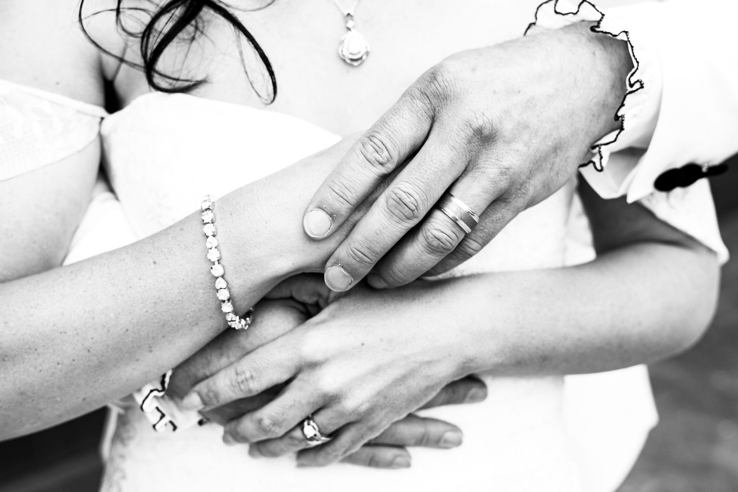 Black and white close-up of hands with wedding rings and bracelets in an intimate moment.