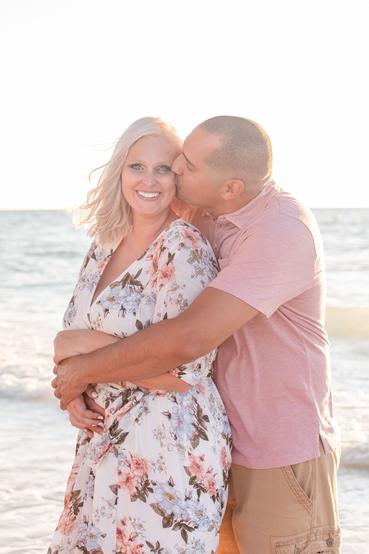 Loving couple sharing intimate moment on beach in pink and floral outfits.