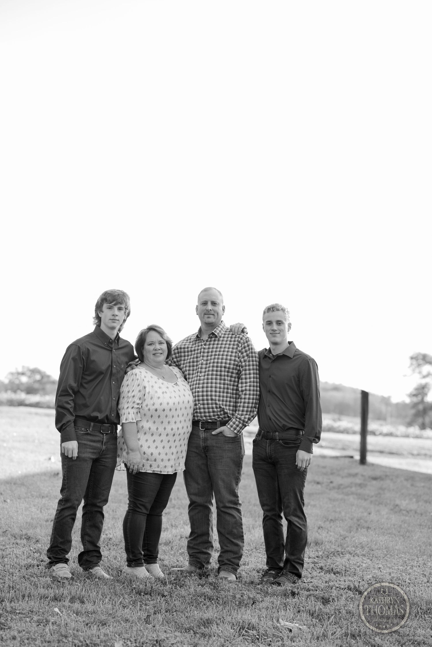 A black and white portrait of a family of four standing together on rural property.