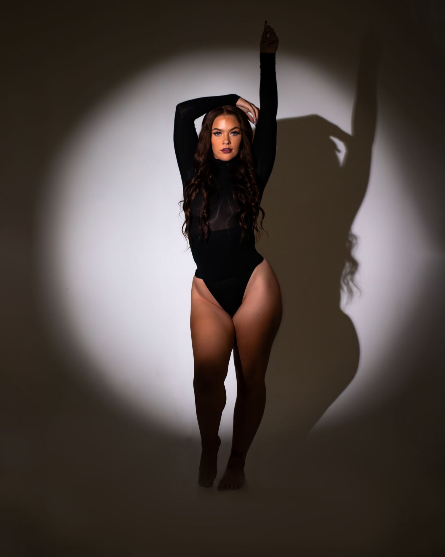 Dramatic spotlight portrait in black bodysuit with shadow effect.
