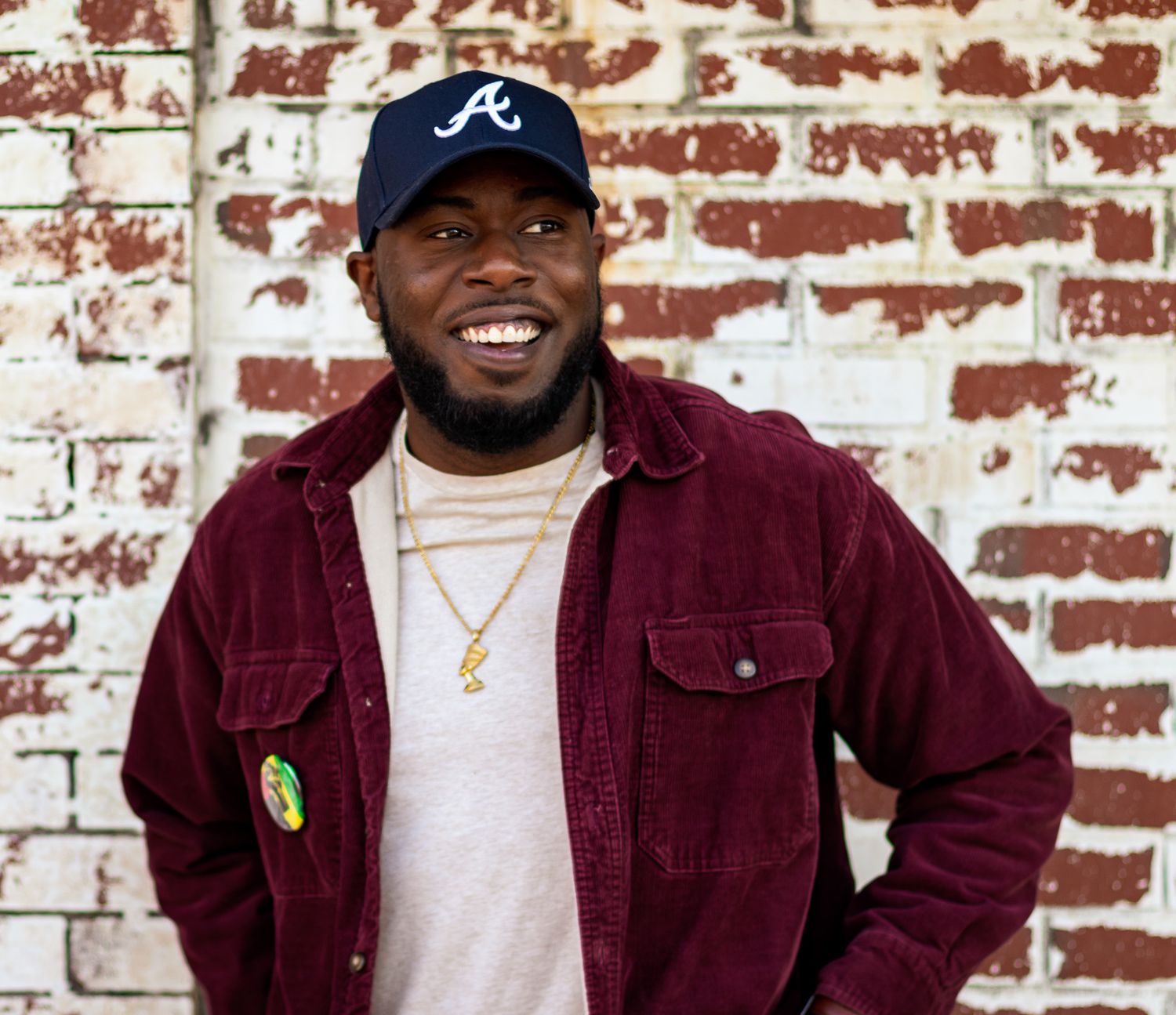 Casual portrait against brick wall wearing Atlanta baseball cap and burgundy corduroy jacket.