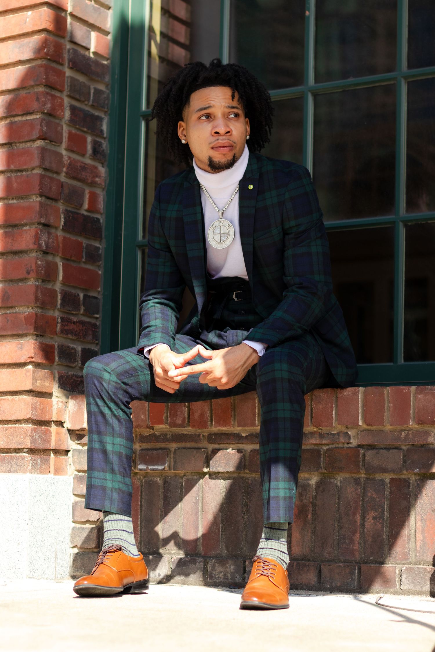 Person in plaid blazer and orange boots sitting on brick ledge in casual pose.