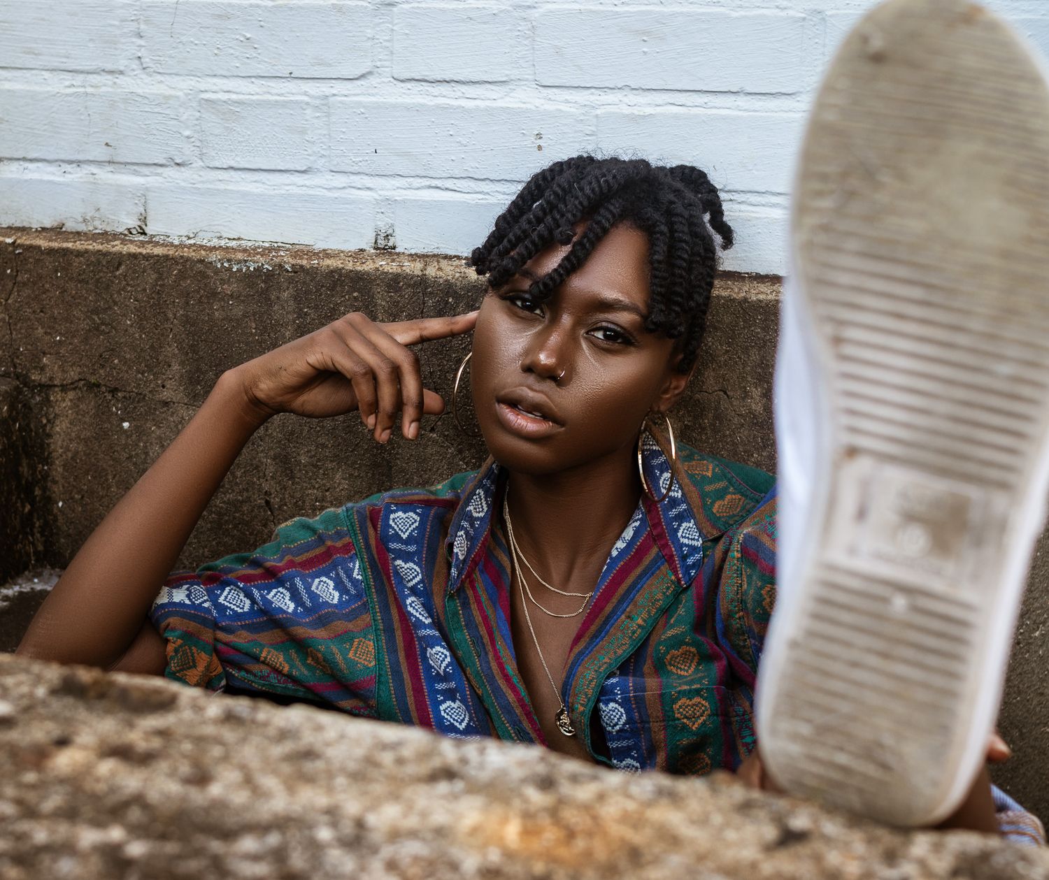 Creative low angle portrait with colorful patterned shirt against white brick wall.
