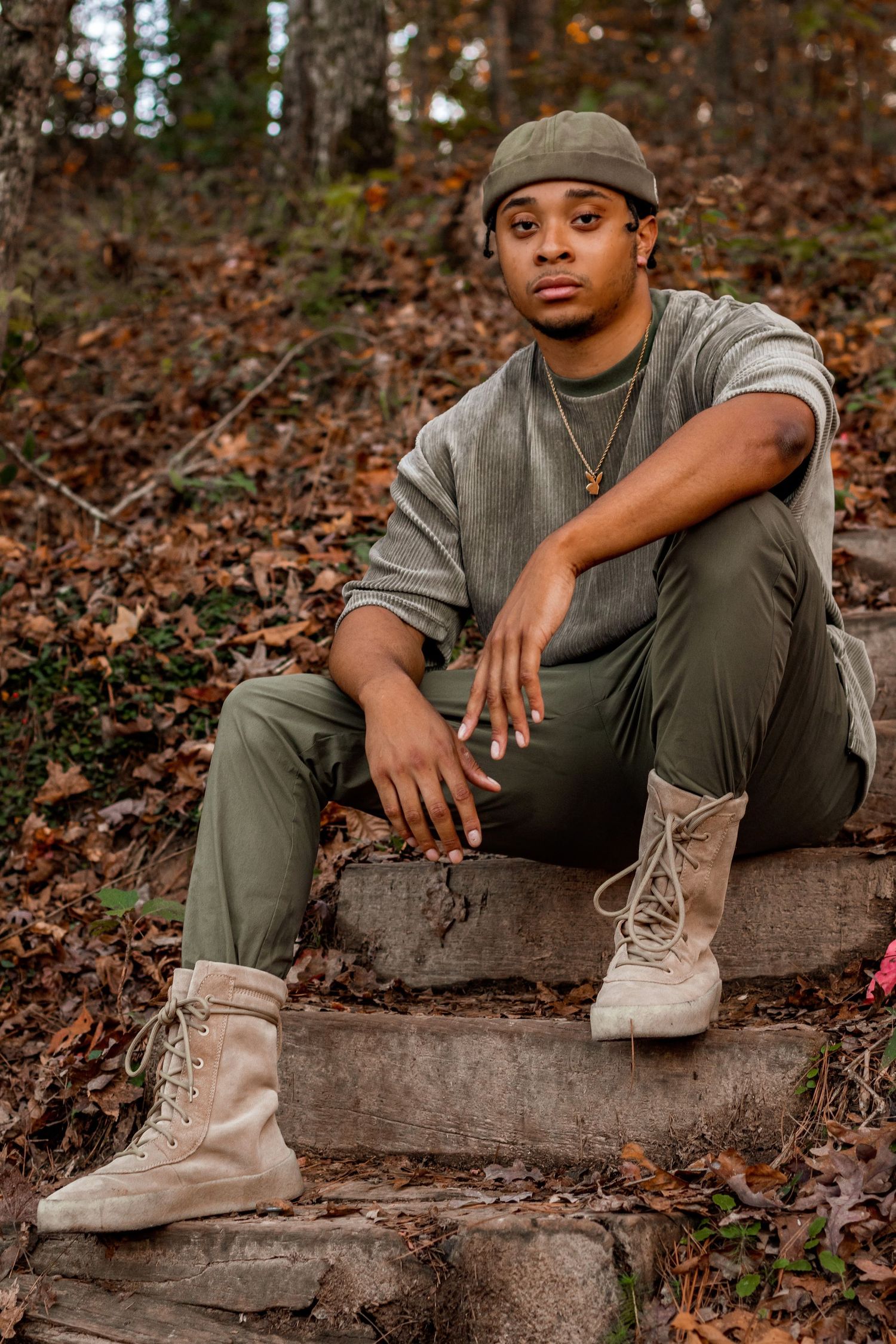 Autumn outdoor portrait of person in neutral tones sitting on stone steps in wooded setting.