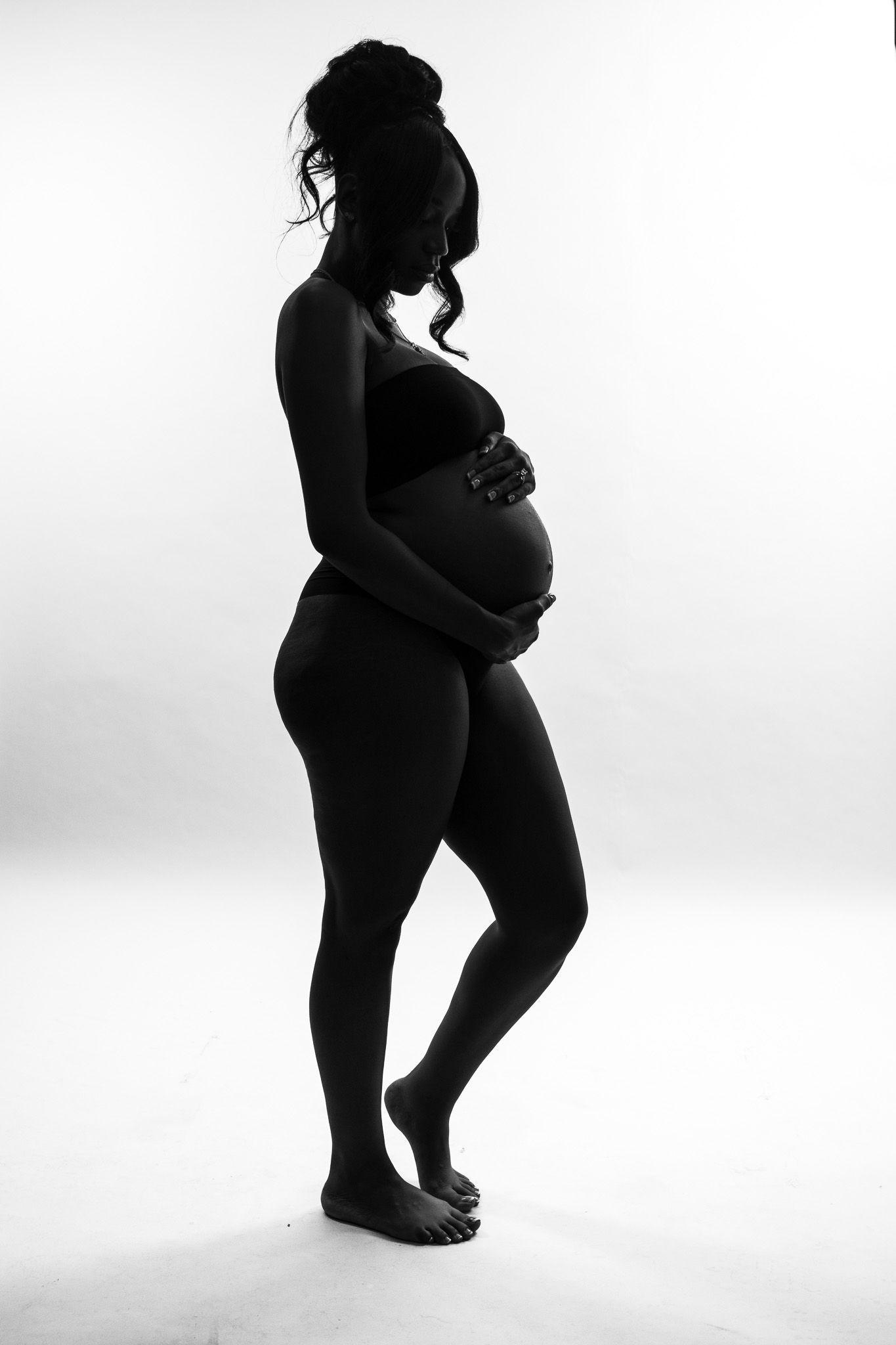 Artistic black and white silhouette of expectant mother against white background.