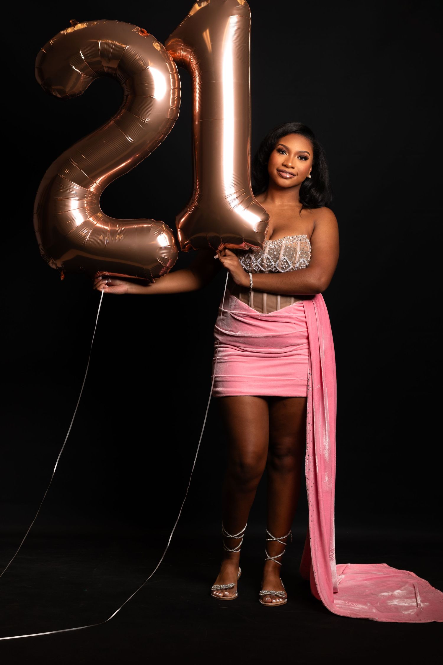 Birthday celebration photo with rose gold number 21 balloons and pink formal dress.