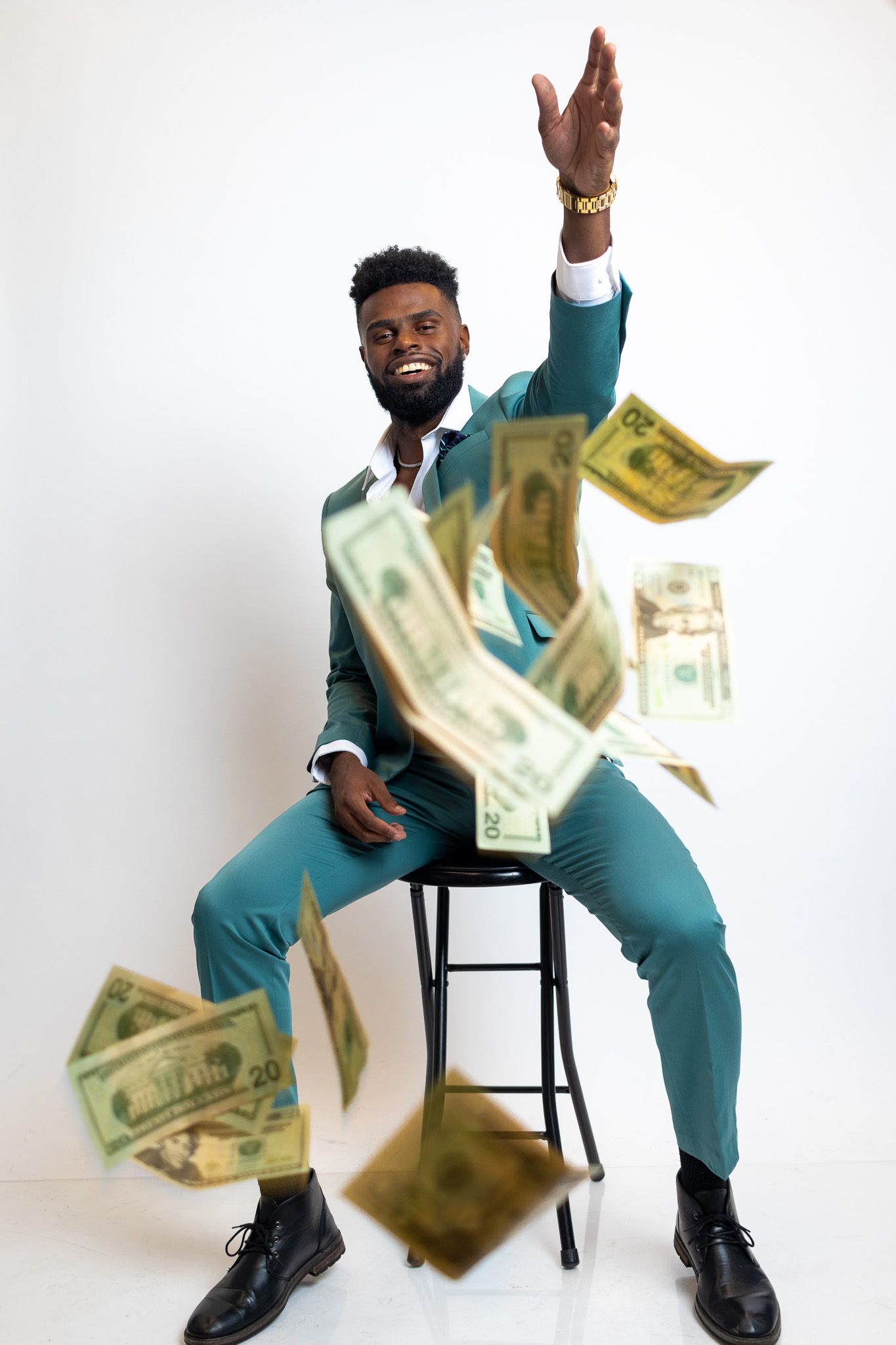 Creative portrait of person in turquoise suit throwing money in the air while sitting on stool.