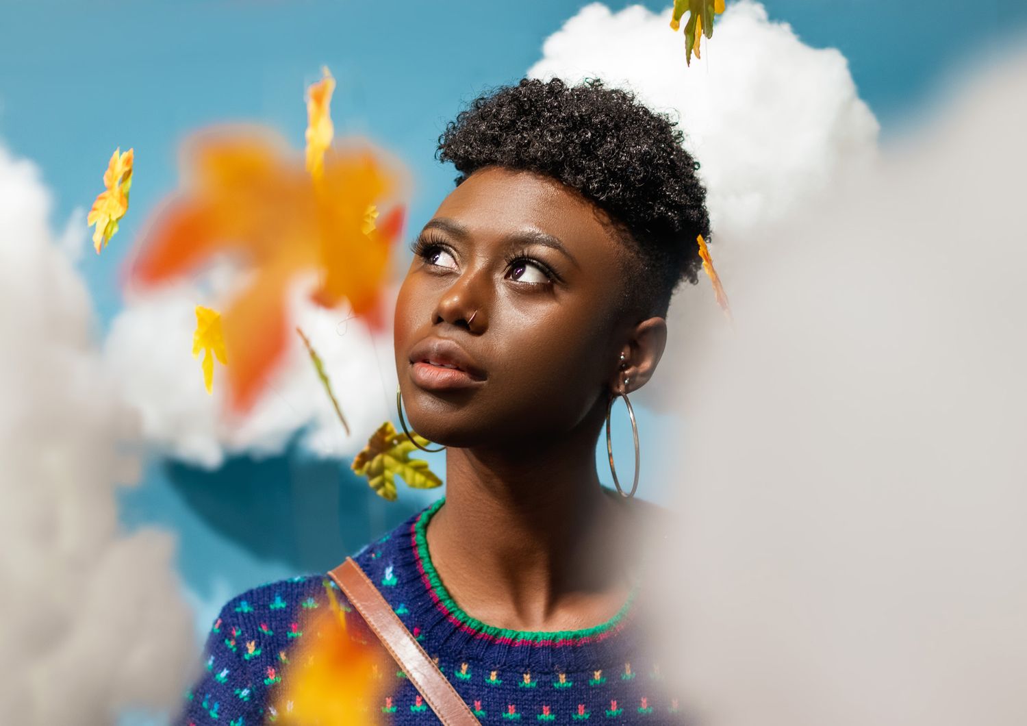 Artistic portrait against blue sky with fall leaves and dreamy bokeh effects.