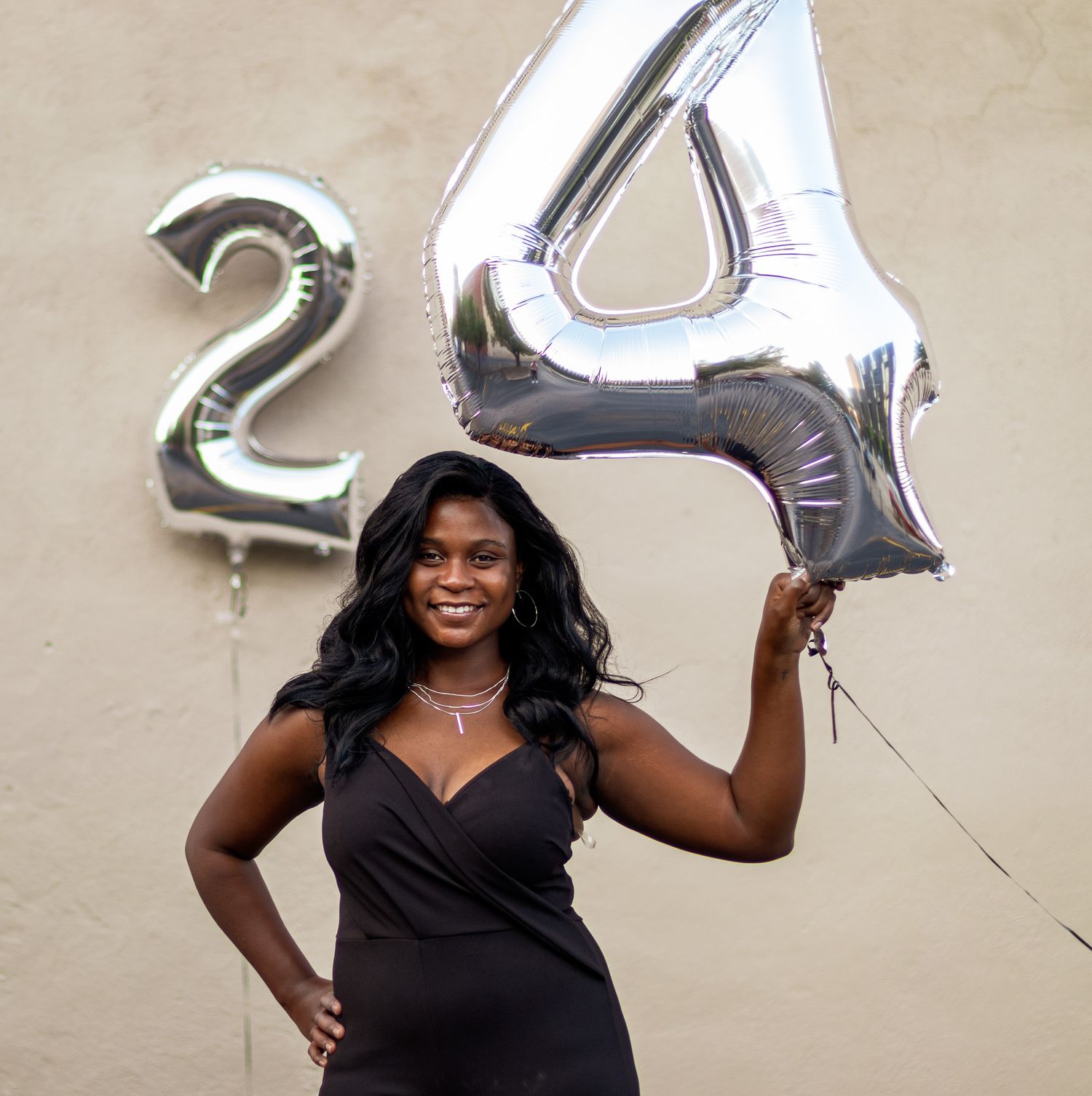 Celebration photo with person in black dress holding silver number 24 balloons.