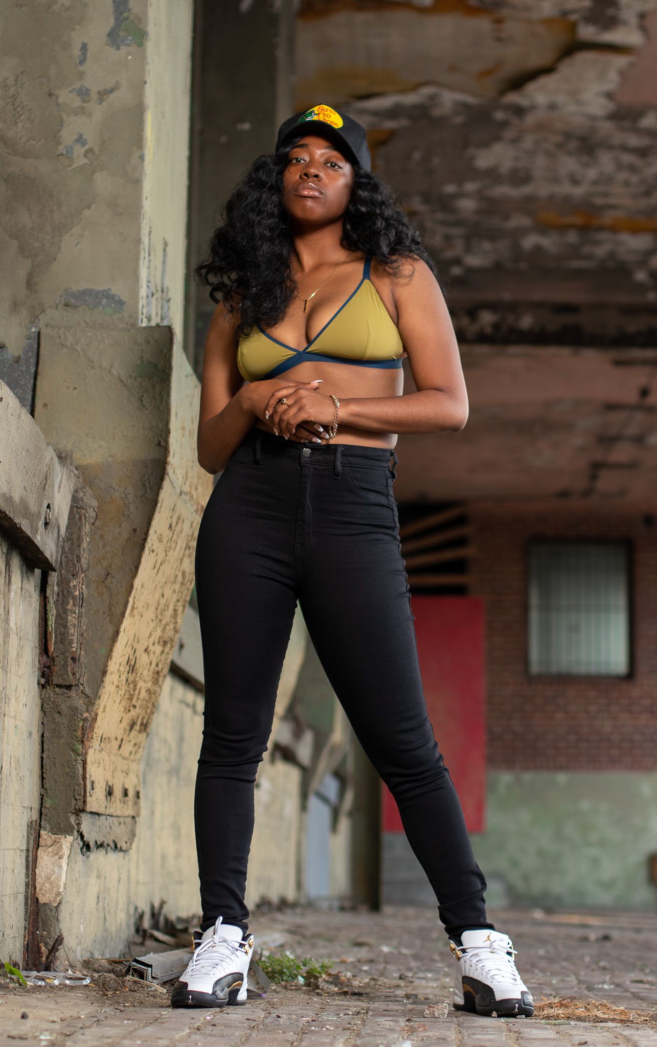 Fashion model wearing yellow crop top and black jeans poses against urban backdrop.