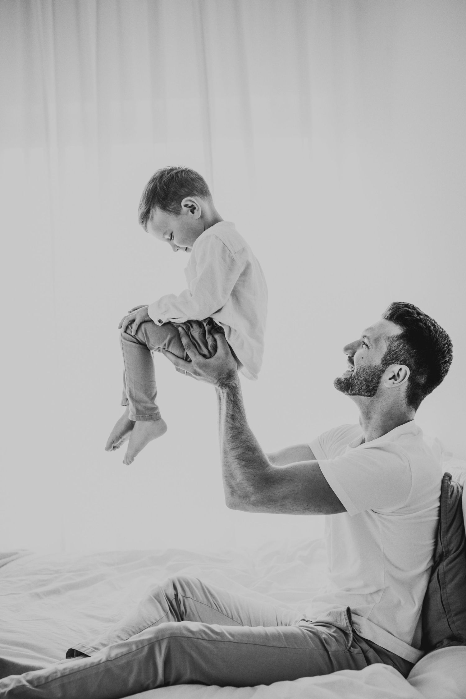Joyful moment between parent and child playing on bed in black and white.