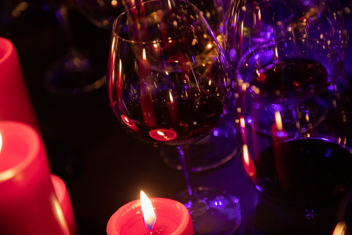 Lit red candles and wine glasses create a romantic ambiance with purple lighting in the background.