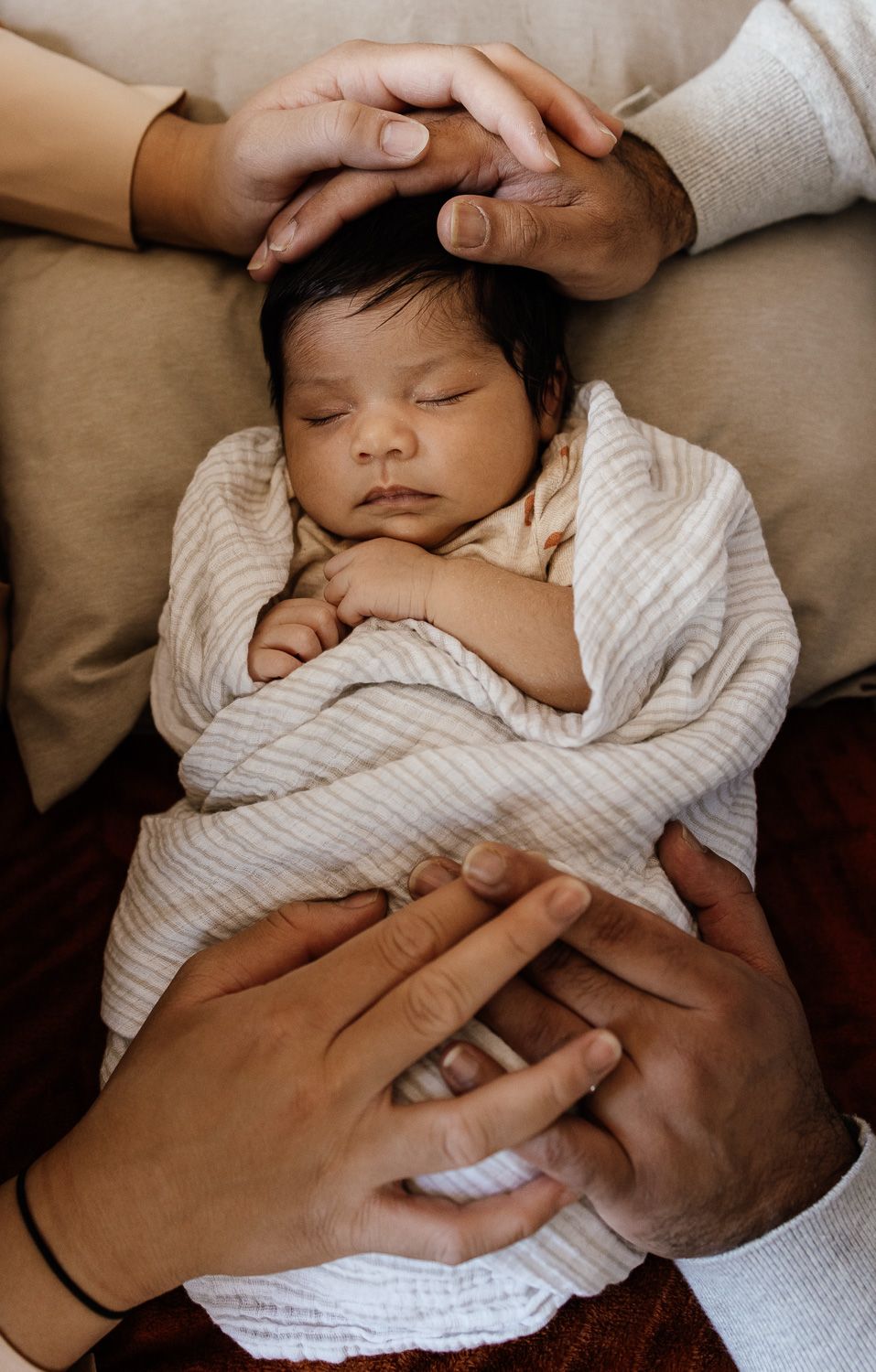 Swaddled newborn baby at an in-home Campbell lifestyle newborn photo session with parents' hands intertwined on the baby