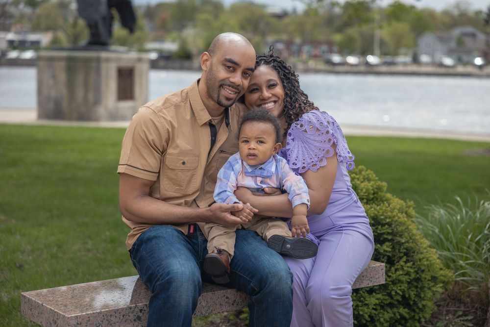 Happy family with mother, father, and baby boy sitting outdoors near waterfront park.