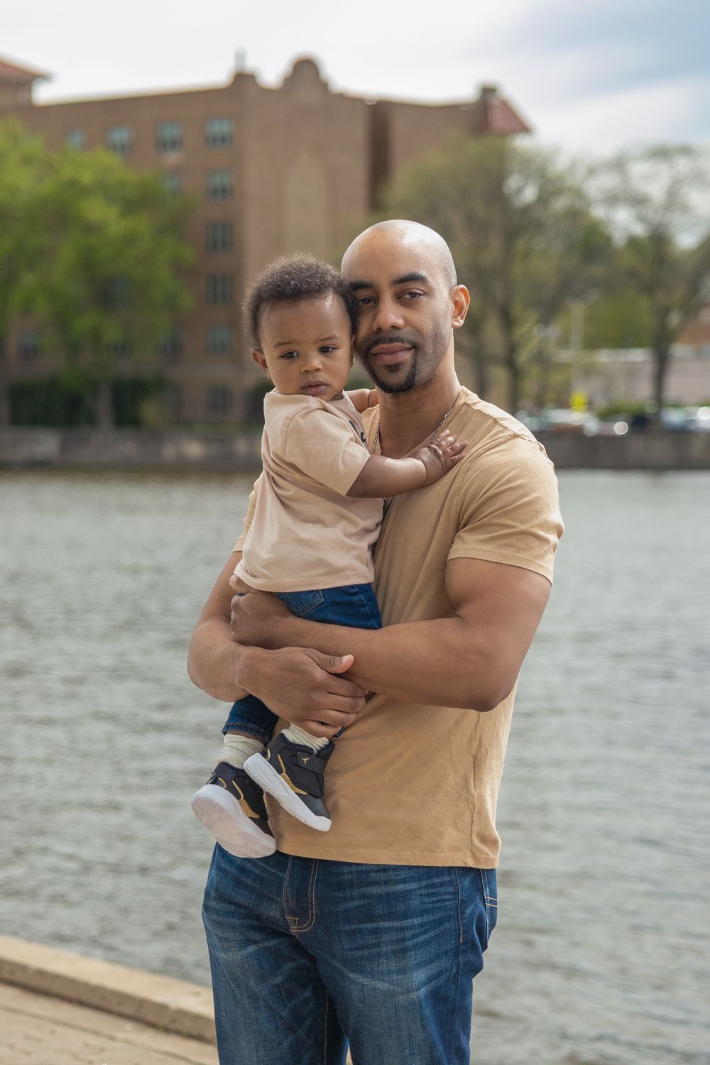 Black father holding his baby son outdoors near a river.