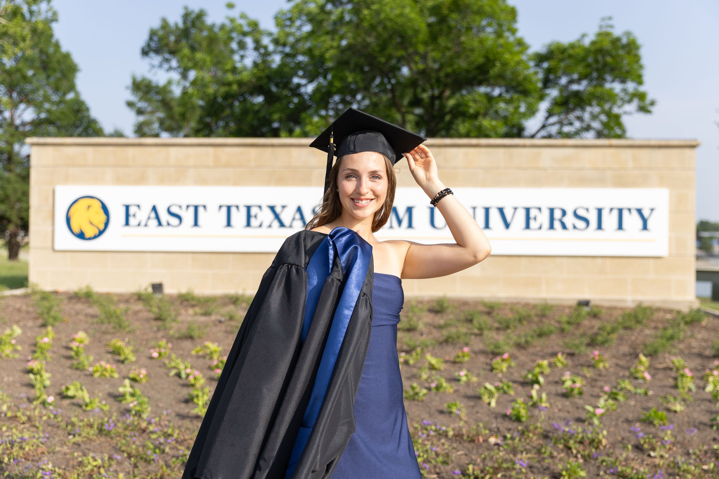 college graduation pictures, girl standing in front of East Texas A&M University sign with cap and gown