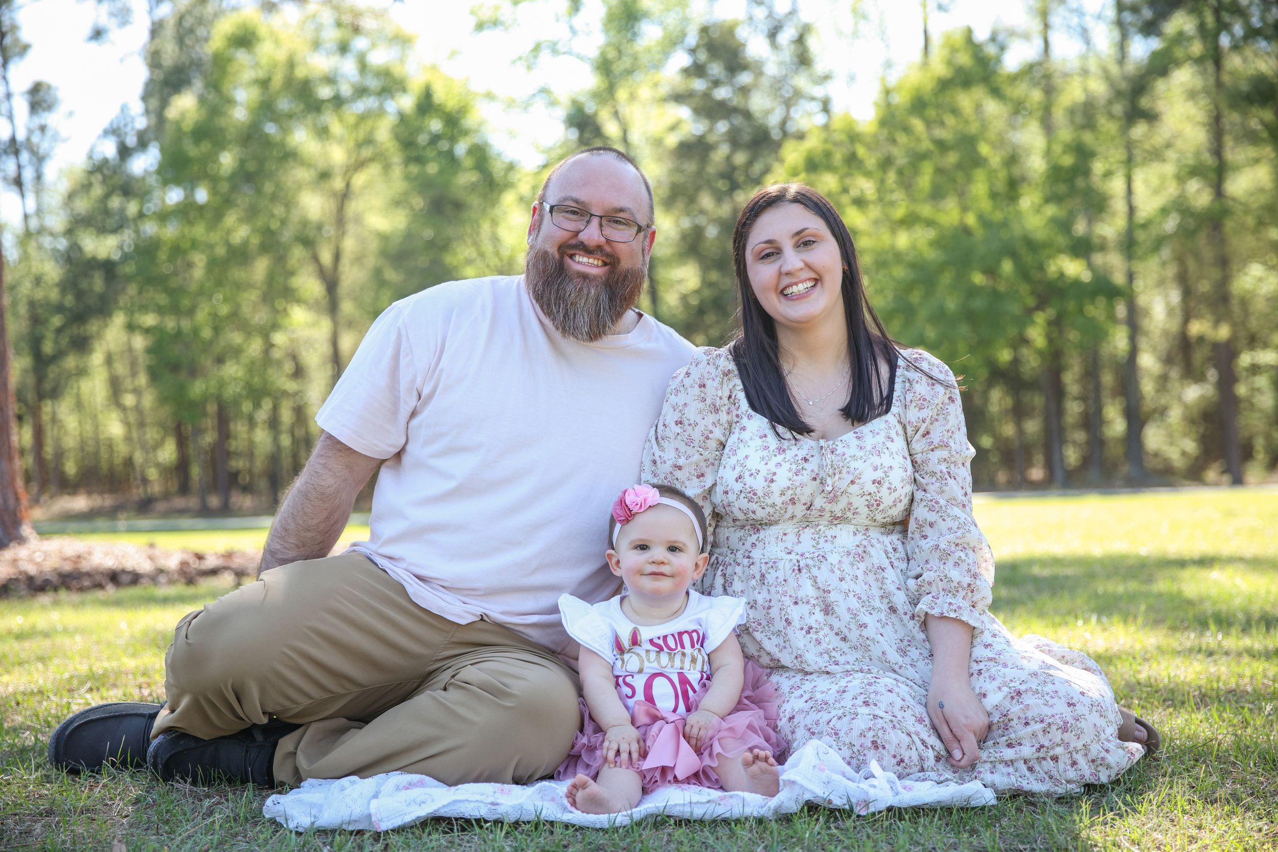 Young mother and father sitting in the ground with their 1 year old baby girl, family portraits at The Boulders, Lake Tyler, Texas