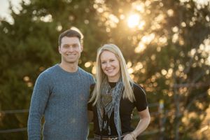 man and woman standing next to each other in front of a tree with sunshine peeking through