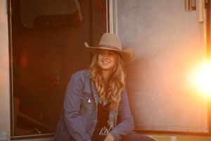 cowgirl lifestyle portrait session sitting in the door of the trailer tack room with sunshine peeking in