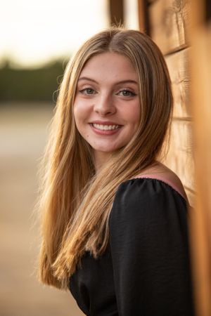 young lady leaning up against a wood wall smiling at the camera