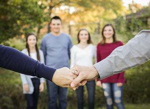 man and woman holding hands with children blurred in the background, family portrait photographer, Tyler, Texas