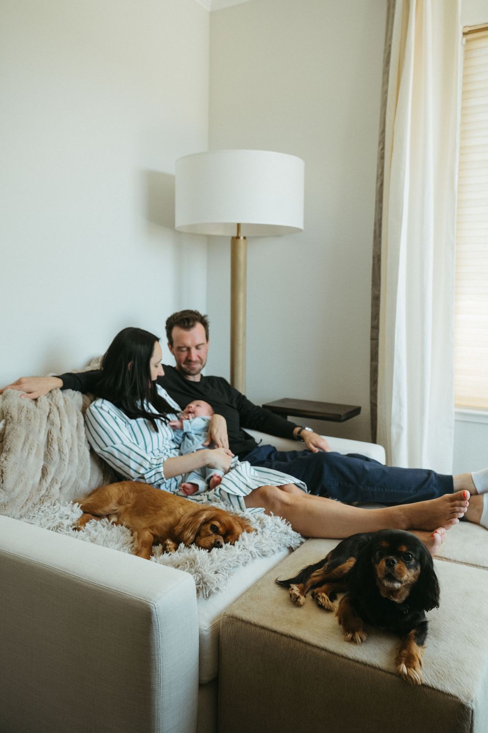 A couple relaxes on a white couch with two dogs while spending quality time together at home.