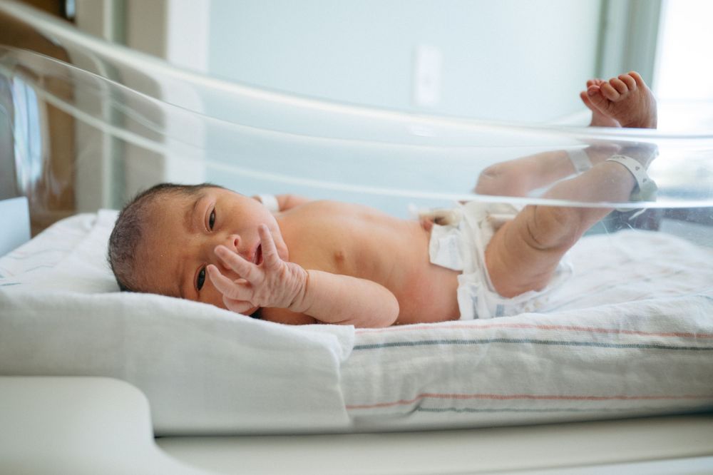 Newborn baby lying in hospital incubator wearing diaper, resting peacefully in neonatal care unit.