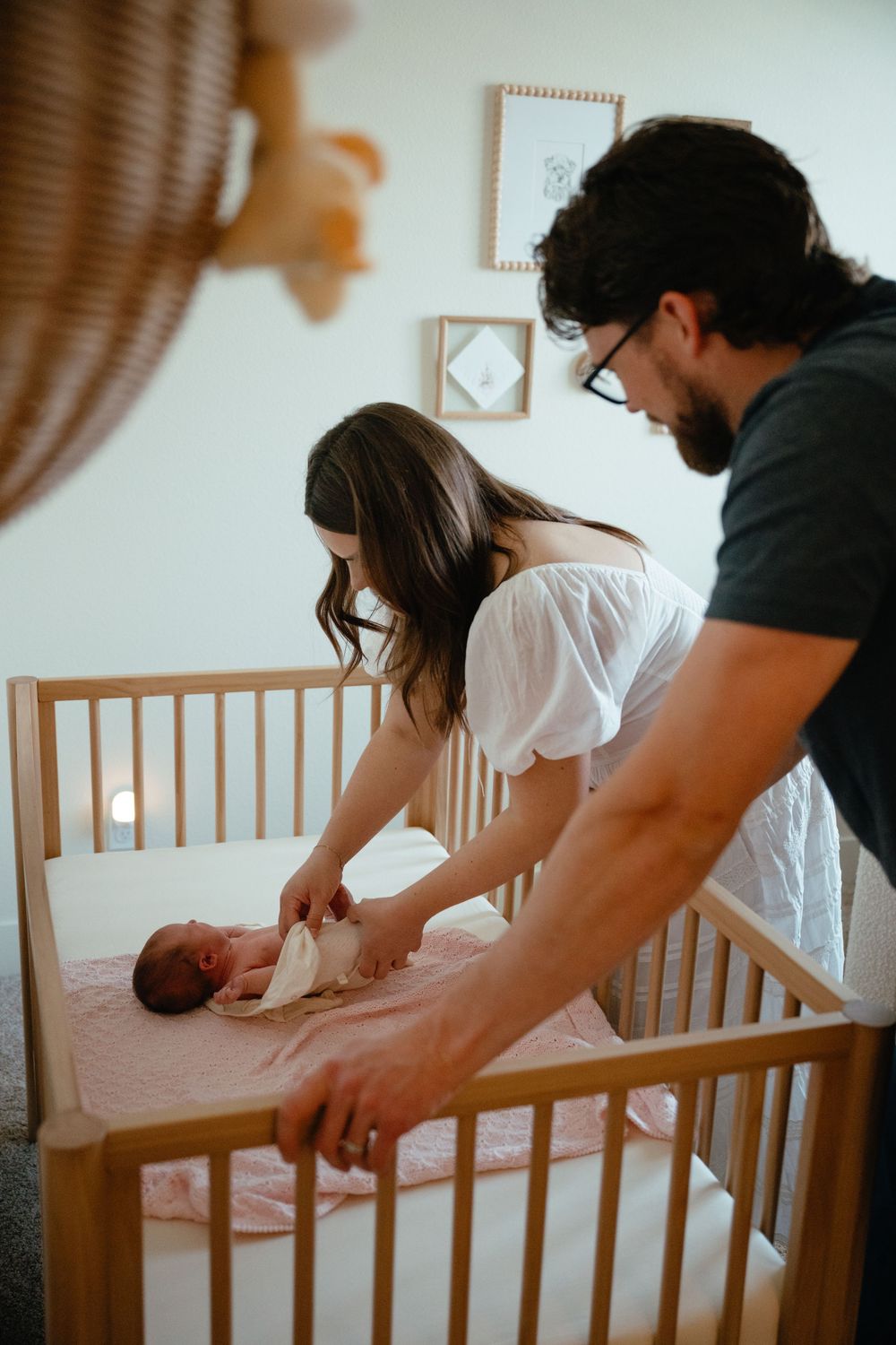 Parents gently placing their newborn baby in a wooden crib in a softly lit nursery room.