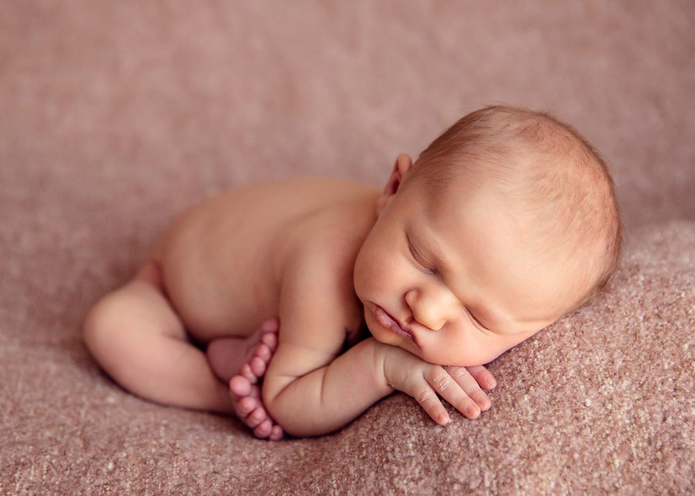 Sleeping newborn posed on soft pink backdrop in natural lighting.