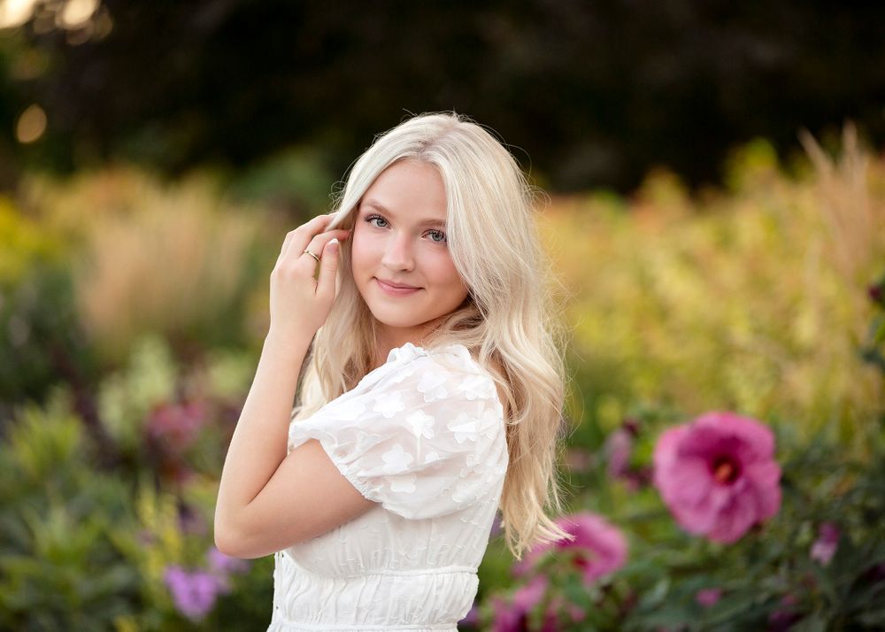 Outdoor portrait in white dress with pink flowers in soft focus background.