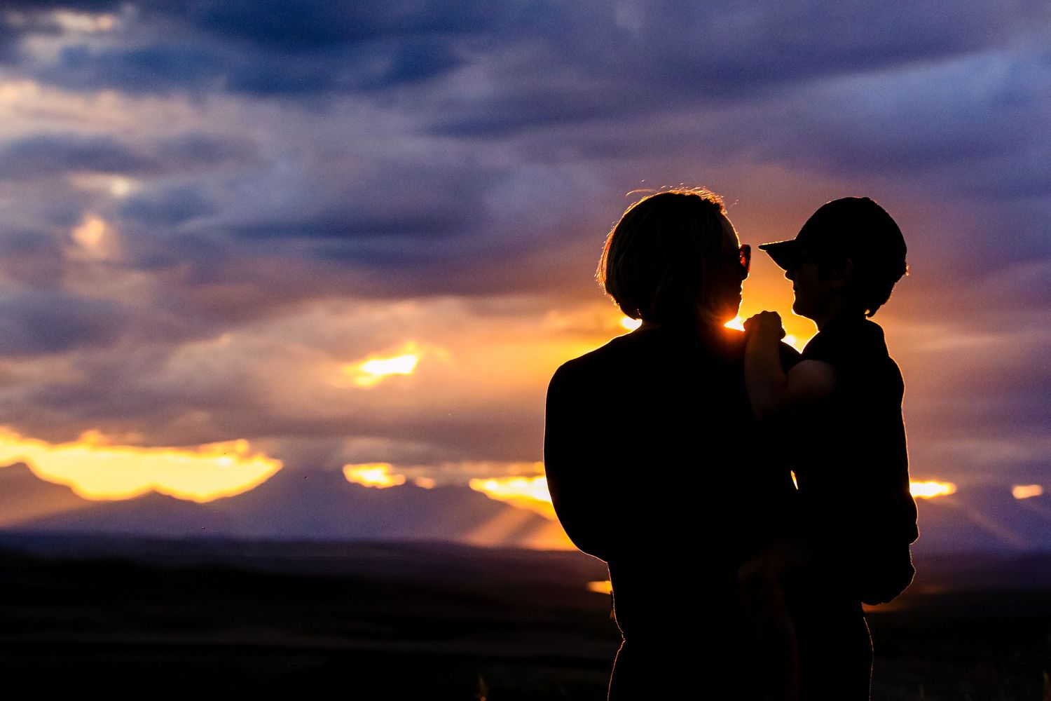 Romantic silhouette of a couple holding a child against a colorful sunset sky.