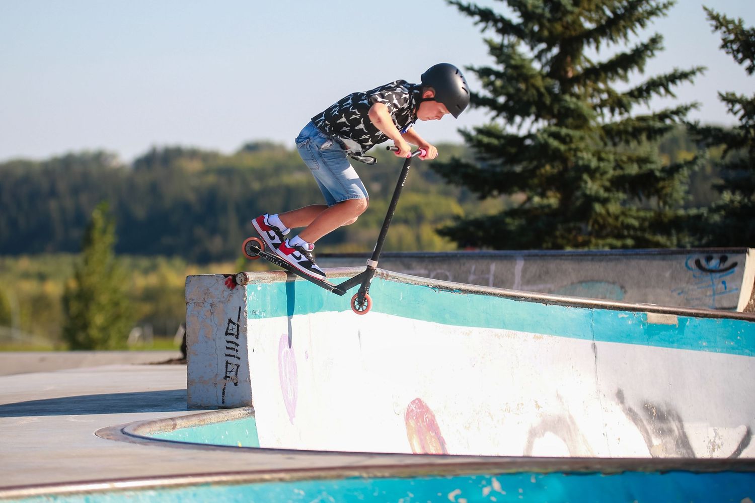 Young skateboarder performing a trick on a scooter at an outdoor skate park.