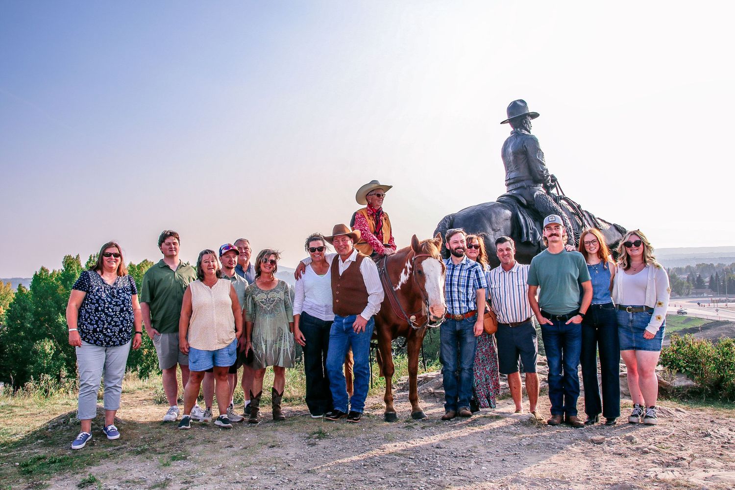 A group of people pose together near a bronze equestrian statue at a scenic outdoor location.