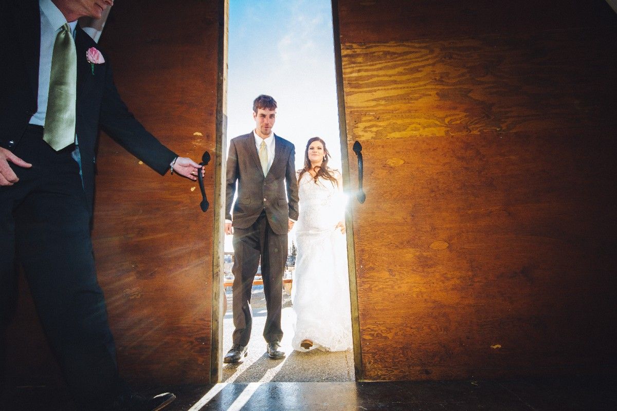 A couple enters through a dramatic doorway bathed in sunlight during their wedding ceremony.