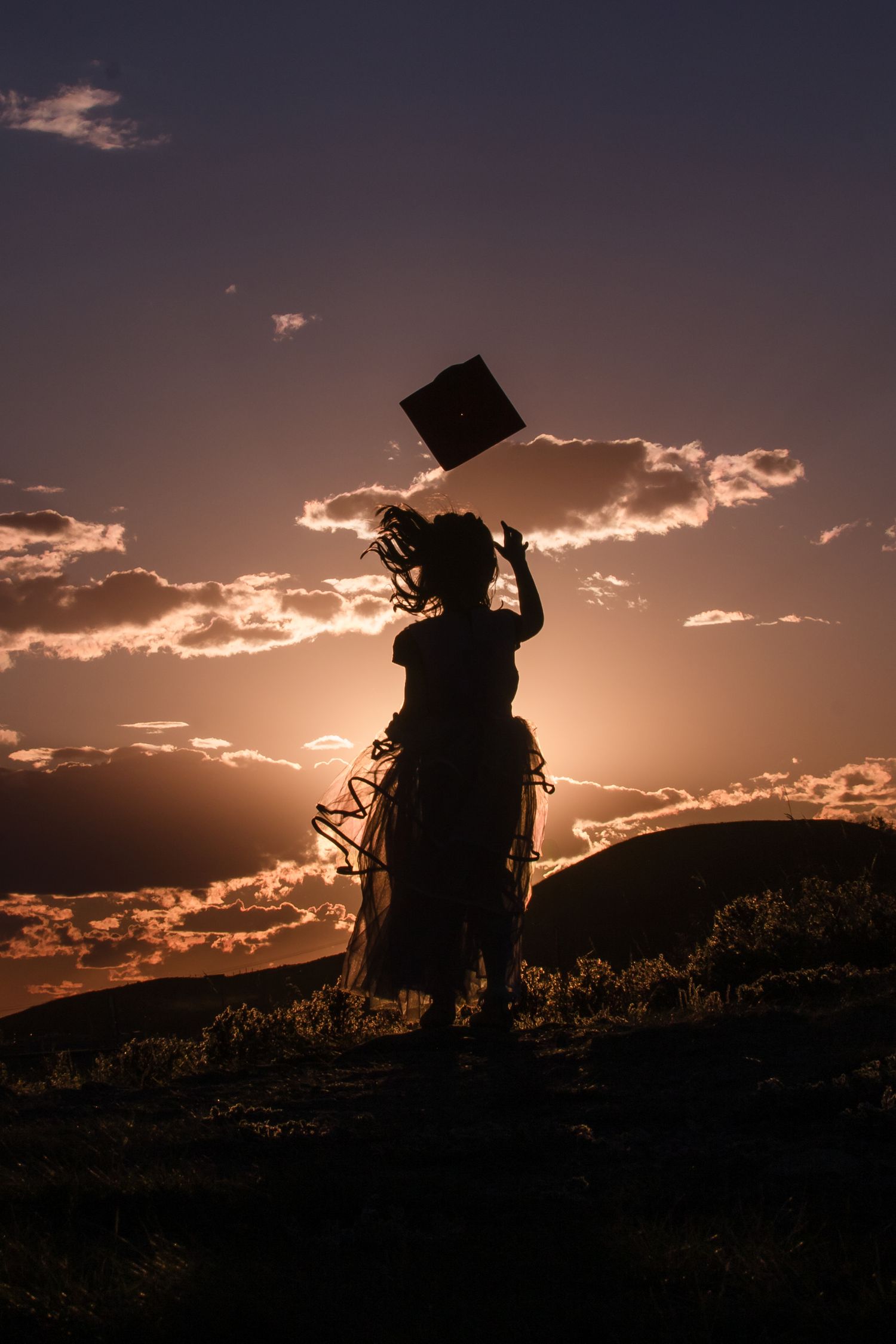 Silhouette of a graduate tossing their cap against a vibrant orange and purple sunset sky.